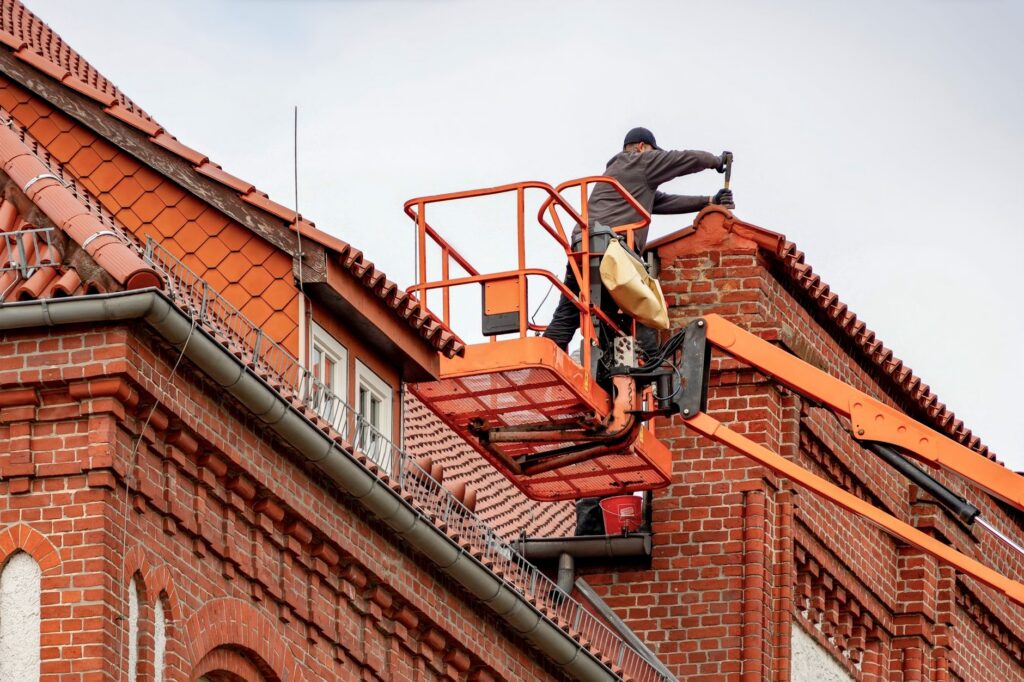 Dakdekker in een hoogwerker bij een pannendak op een bakstenen gebouw