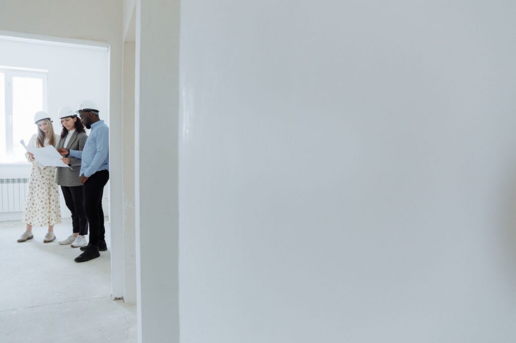 Drie mensen met bouwhelmen in een lege, witte ruimte