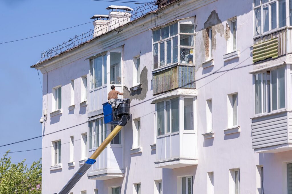 Schilder in een hoogwerker bij een witte flatgevel