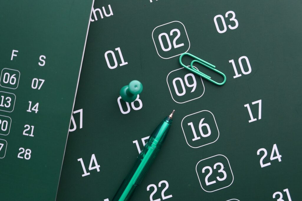 Groene kalender met pen, punaise en paperclip