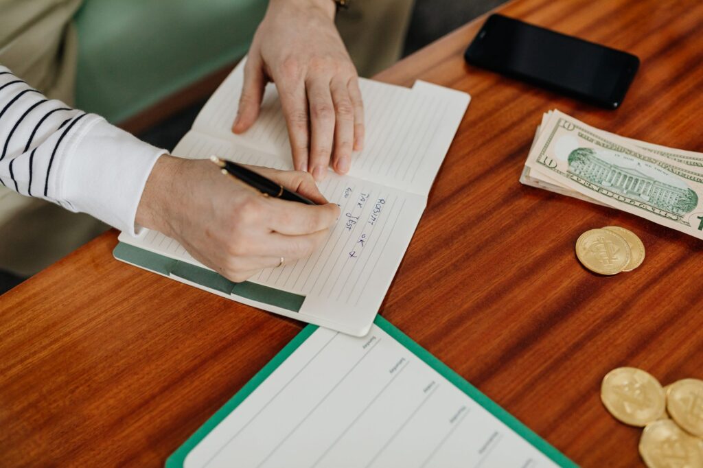 Iemand schrijft in een notitieboek naast bankbiljetten en munten